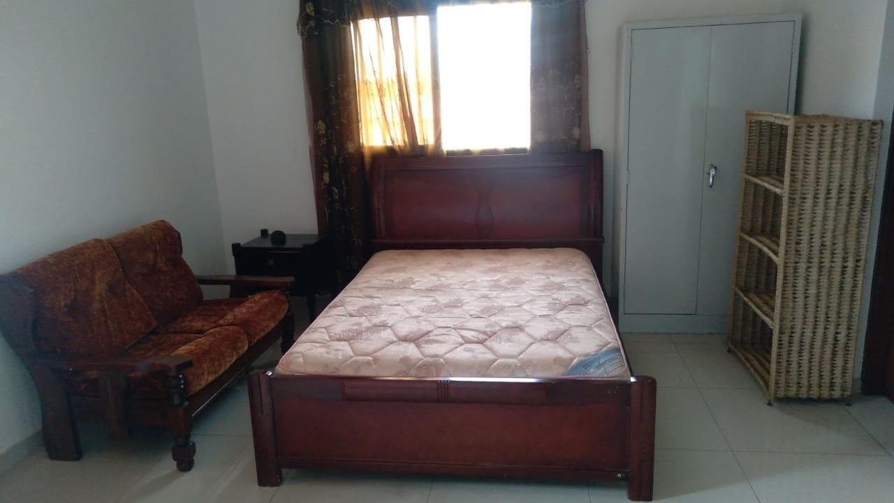 Cama de casal, cabeceira, cacifo metálico, estante de palha e um sofá ·
